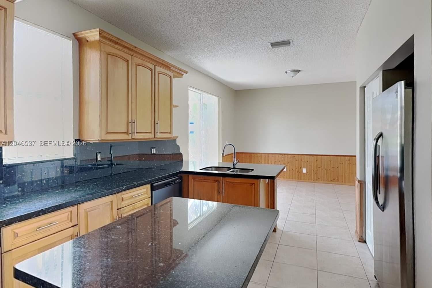 A kitchen features wood cabinets, black granite countertops, a central island, and tile flooring — WESTON, FL