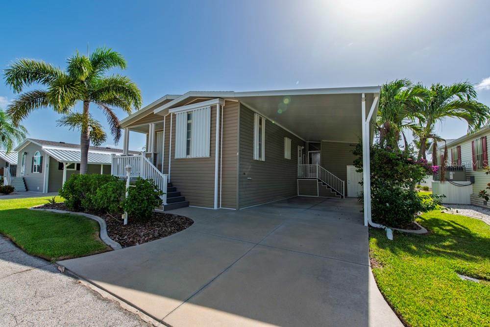 A tan manufactured home features a concrete driveway, a covered carport, and a front porch — 31 COPENHAGEN AVENUE, PUNTA GORDA, FL
