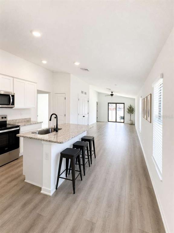 A kitchen with white cabinets and a granite island overlooks a long, open-concept living area — 5668 FLOTILLA AVENUE, TAMPA, FL