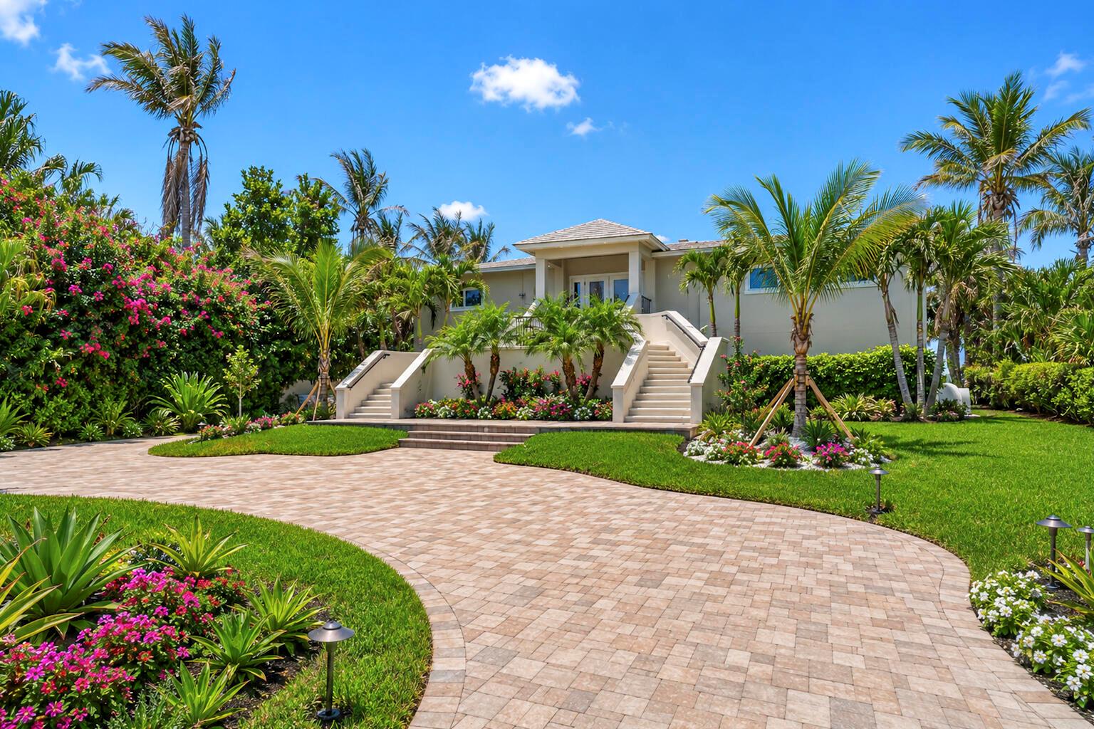 A beige house with dual staircases and a paved driveway surrounded by lush tropical landscaping — VERO BEACH, FL