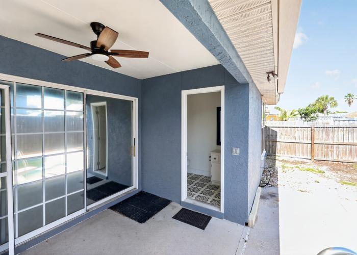 A covered patio with a ceiling fan, sliding glass doors, and an exterior bathroom entrance — 104 SEASHELL COURT, PANAMA CITY BEACH, FL