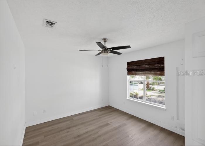 An empty bedroom with white walls, wood-look flooring, a ceiling fan, and a window — 104 SEASHELL COURT, PANAMA CITY BEACH, FL