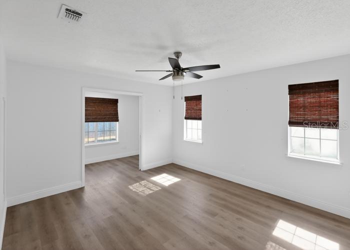 An empty bedroom with white walls, wood-look flooring, a ceiling fan, and three windows — 104 SEASHELL COURT, PANAMA CITY BEACH, FL