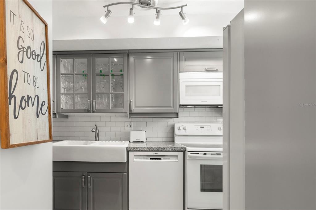 A kitchen features gray cabinets, white appliances, a farmhouse sink, and a subway tile backsplash — 400 GLENNES LANE UNIT 107, DUNEDIN, FL