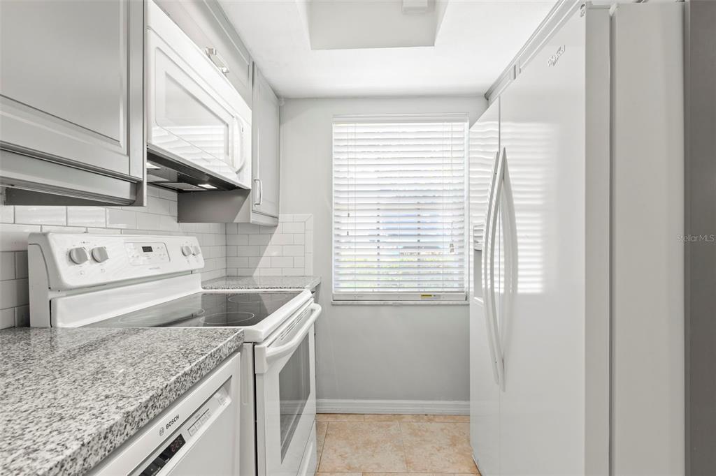 A galley kitchen features white cabinets, granite countertops, a white stove, and a white refrigerator — 400 GLENNES LANE UNIT 107, DUNEDIN, FL