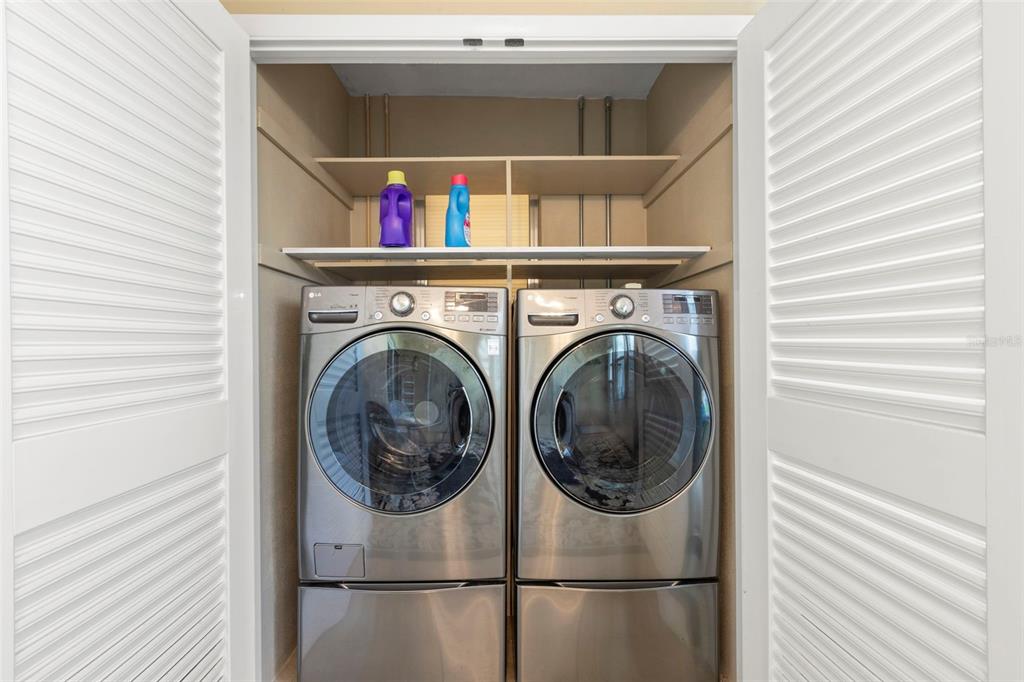 A laundry closet features a side-by-side washer and dryer with shelving above — 400 GLENNES LANE UNIT 107, DUNEDIN, FL