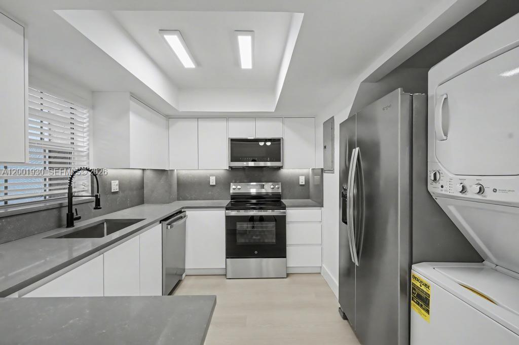 A modern kitchen features white cabinets, stainless steel appliances, gray countertops, and a stacked washer-dryer — 12224 SW 52nd Pl, Cooper City FL 33330, COOPER CITY, FL
