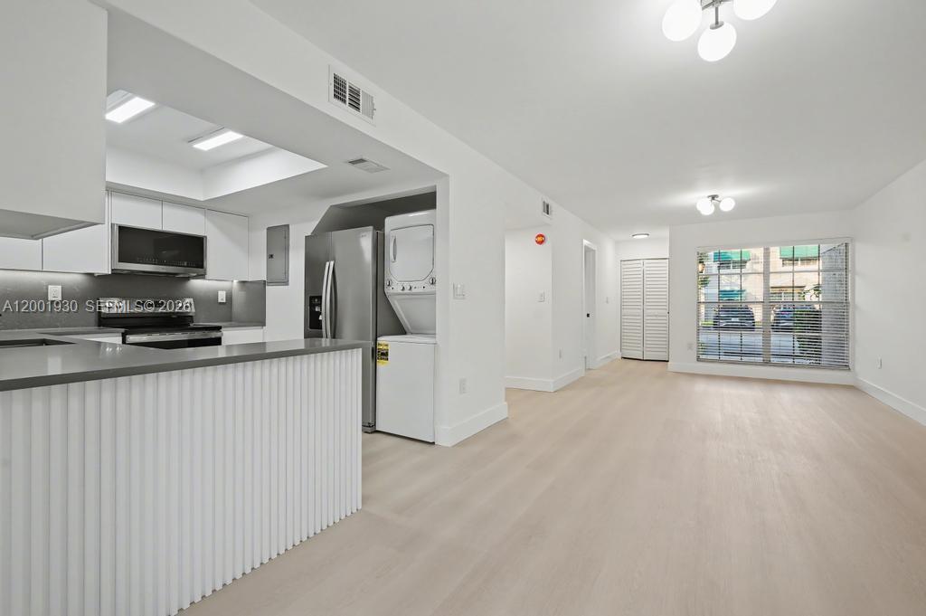 A modern kitchen with white cabinets and a stacked washer-dryer opens to a living area — 12224 SW 52nd Pl, Cooper City FL 33330, COOPER CITY, FL