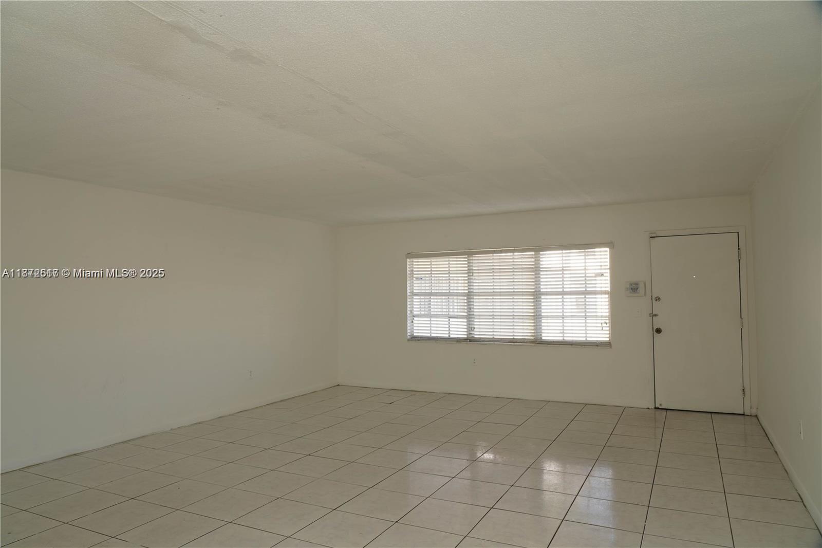 An empty room features white walls, a tiled floor, and a window with blinds — 11855 NE 19th Dr # 10, North Miami FL 33181, NORTH MIAMI, FL