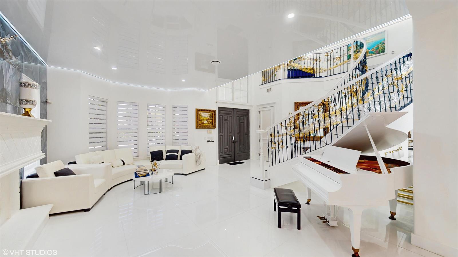 A bright, white-tiled foyer features a grand staircase, a white piano, and modern seating — 377 Squire Drive, Wellington FL 33414, WELLINGTON, FL