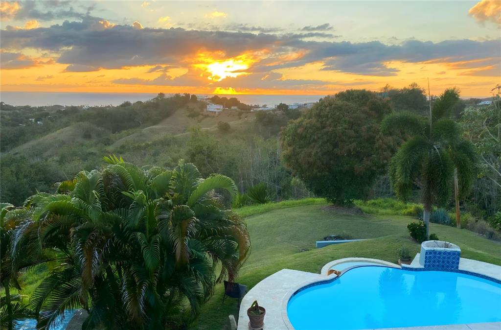A swimming pool overlooks a grassy hillside and the ocean during a sunset — VILLA DE SUENOS SECTOR KOREA, RINCON, PR