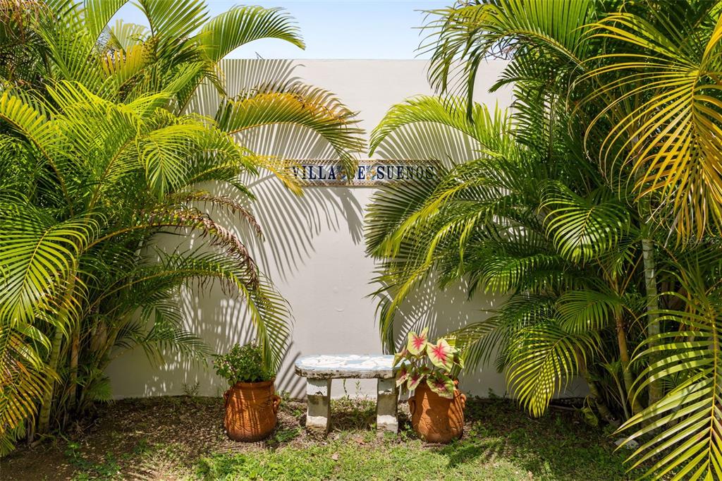 A stone bench sits between two potted plants against a wall with a name sign — VILLA DE SUENOS SECTOR KOREA, RINCON, PR