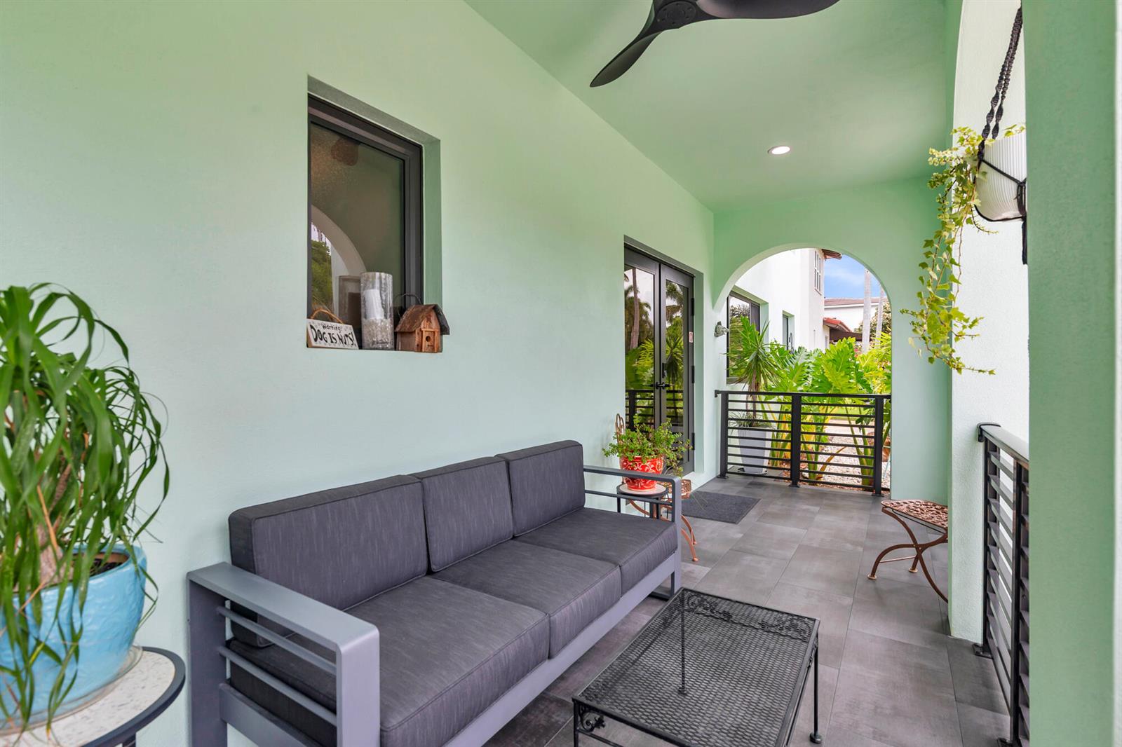 A covered outdoor balcony features light green walls, a dark sofa, a metal coffee table, and tile flooring — 127 Auburn Drive, FL 33460, FL