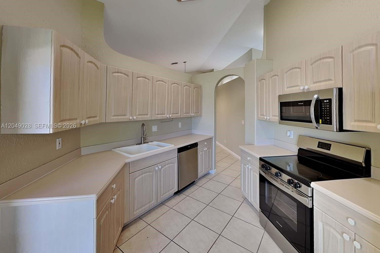 A kitchen features light wood cabinets, white countertops, tile flooring, and stainless steel appliances — DELRAY BEACH, FL