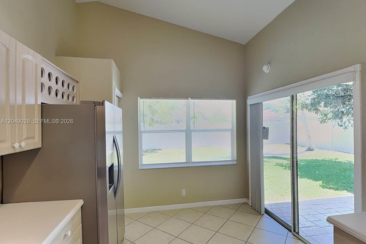 A kitchen with light-colored cabinets, a stainless steel refrigerator, tile flooring, and sliding glass doors — DELRAY BEACH, FL
