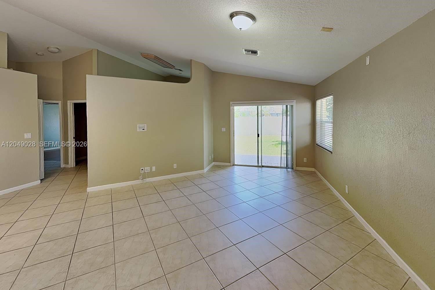 An empty living room features beige tile flooring, vaulted ceilings, and sliding glass patio doors — DELRAY BEACH, FL