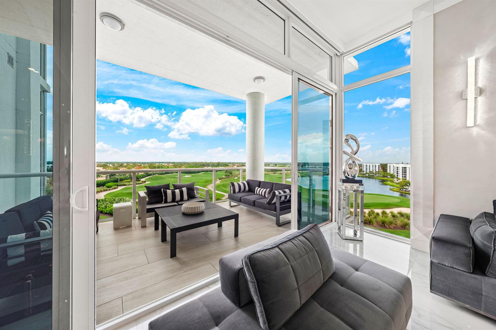A modern living room opens through sliding glass doors to a balcony overlooking a golf course — 20155 Boca West Drive # B804, Boca Raton FL 33434, BOCA RATON, FL