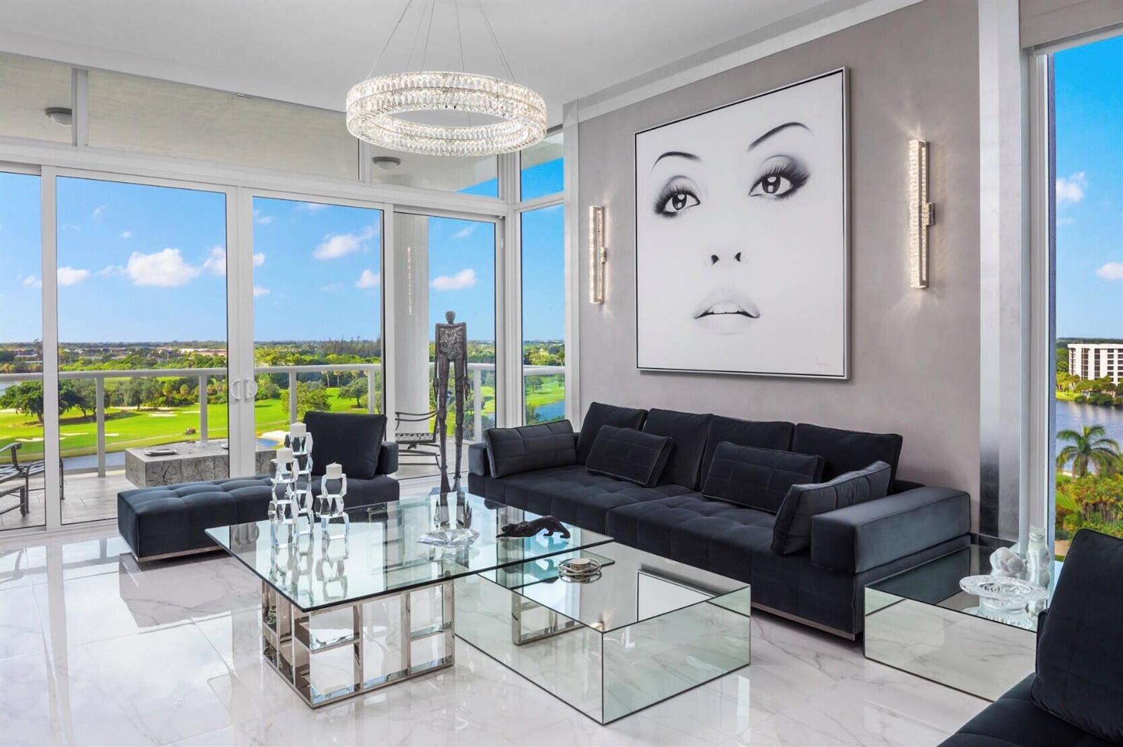 A modern living room features a black sofa, glass coffee tables, and a large portrait painting — 20155 Boca West Drive # B804, Boca Raton FL 33434, BOCA RATON, FL