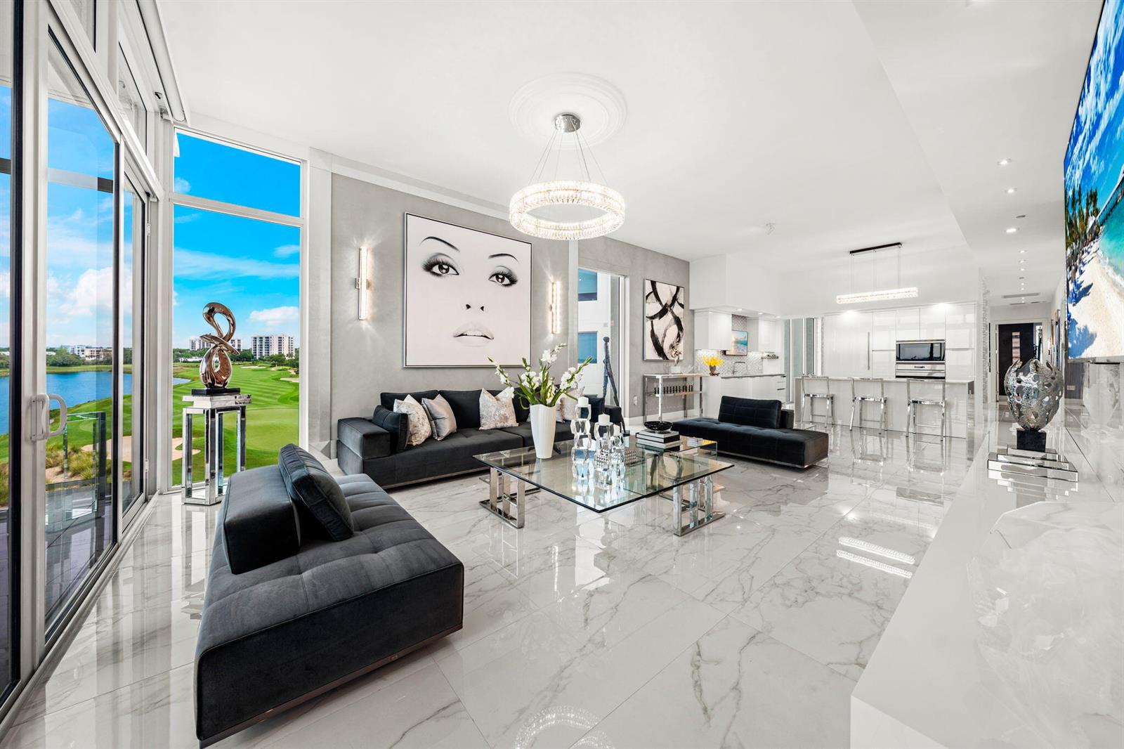 A modern living room with marble floors, dark sofas, and a view of a golf course — 20155 Boca West Drive # B804, Boca Raton FL 33434, BOCA RATON, FL