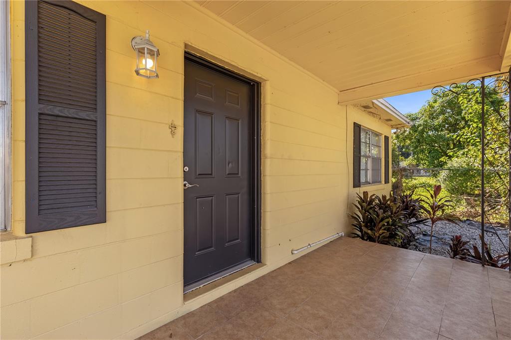 A covered porch with tiled flooring leads to a dark front door on a yellow house — 309 N 22ND STREET, TAMPA, FL