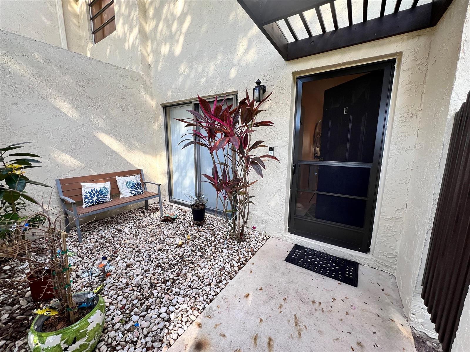 A patio area features a bench, a potted plant, and a front door with a screen — 8460 Casa Del Lago, Boca Raton FL 33433, BOCA RATON, FL