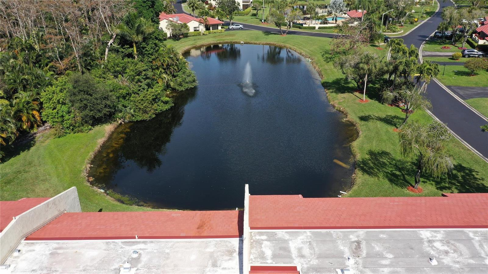 An aerial view shows a pond with a fountain behind a building with a roof — 8460 Casa Del Lago, Boca Raton FL 33433, BOCA RATON, FL