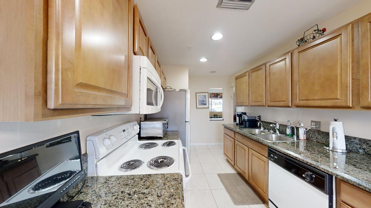 A kitchen features wood cabinets, granite countertops, white appliances, and light-colored tile flooring — 8460 Casa Del Lago, Boca Raton FL 33433, BOCA RATON, FL