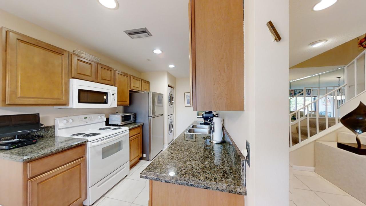 A kitchen with wood cabinets, granite countertops, white appliances, and a view of a staircase — 8460 Casa Del Lago, Boca Raton FL 33433, BOCA RATON, FL