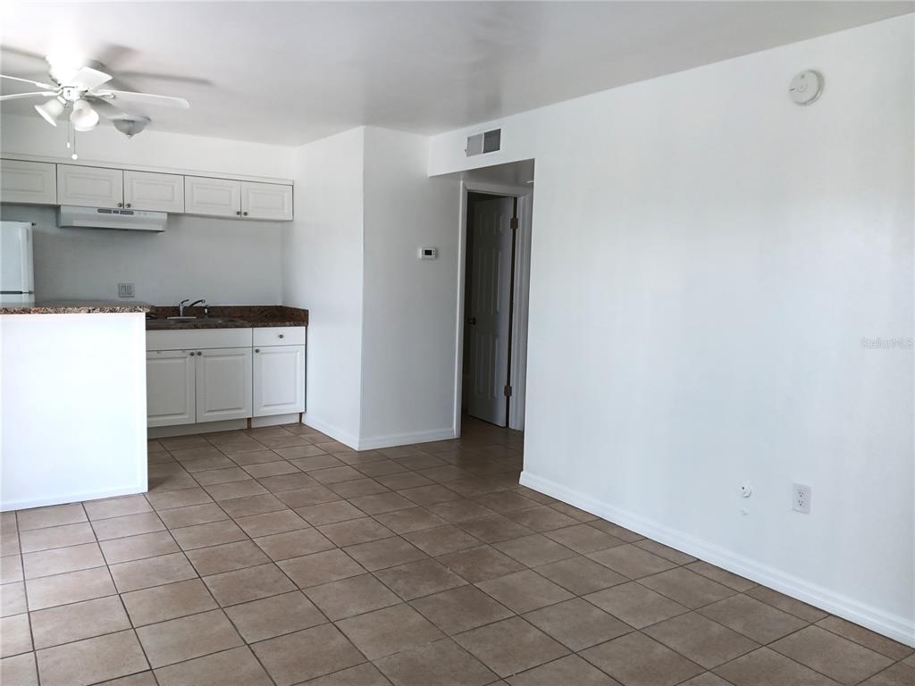 A kitchen with white cabinets and tile flooring opens into a living area — 885 BELTREES STREET UNIT 7, DUNEDIN, FL