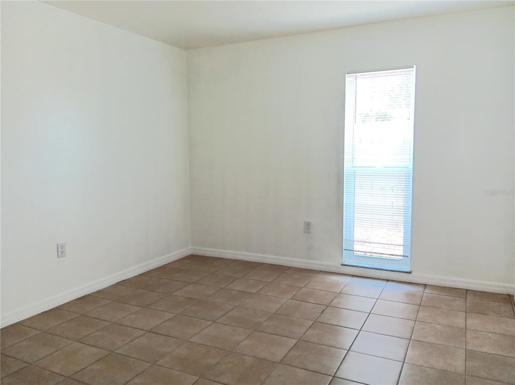An empty room features white walls, tan tile flooring, and a single window with blinds — 885 BELTREES STREET UNIT 7, DUNEDIN, FL