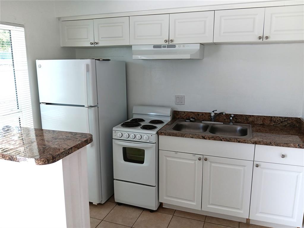 A kitchen features white cabinets, a white refrigerator, a white stove, and granite countertops — 885 BELTREES STREET UNIT 7, DUNEDIN, FL