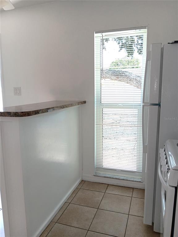 A kitchen features a breakfast bar, tiled flooring, a window with blinds, and a refrigerator — 885 BELTREES STREET UNIT 7, DUNEDIN, FL