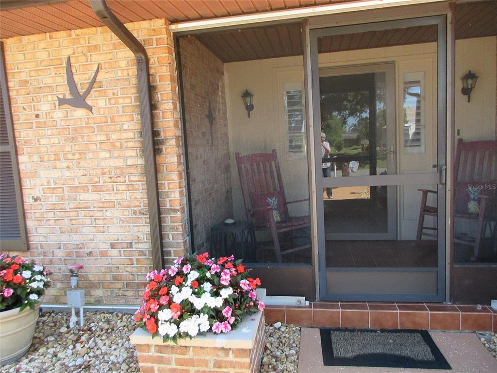 A brick-walled porch features a screened door, two rocking chairs, and potted flowers — 4110 ALLURE LANE, NORTH PORT, FL
