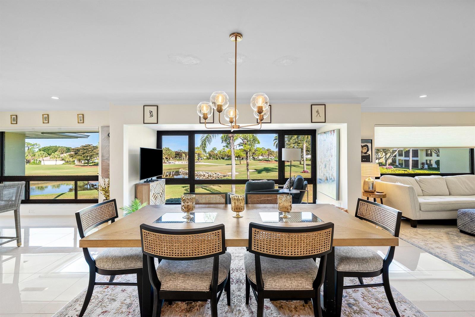 A dining room with a wooden table and cane chairs overlooks a golf course and pond — 3637 Quail Ridge Drive # A, Boynton Beach FL 33436, BOYNTON BEACH, FL