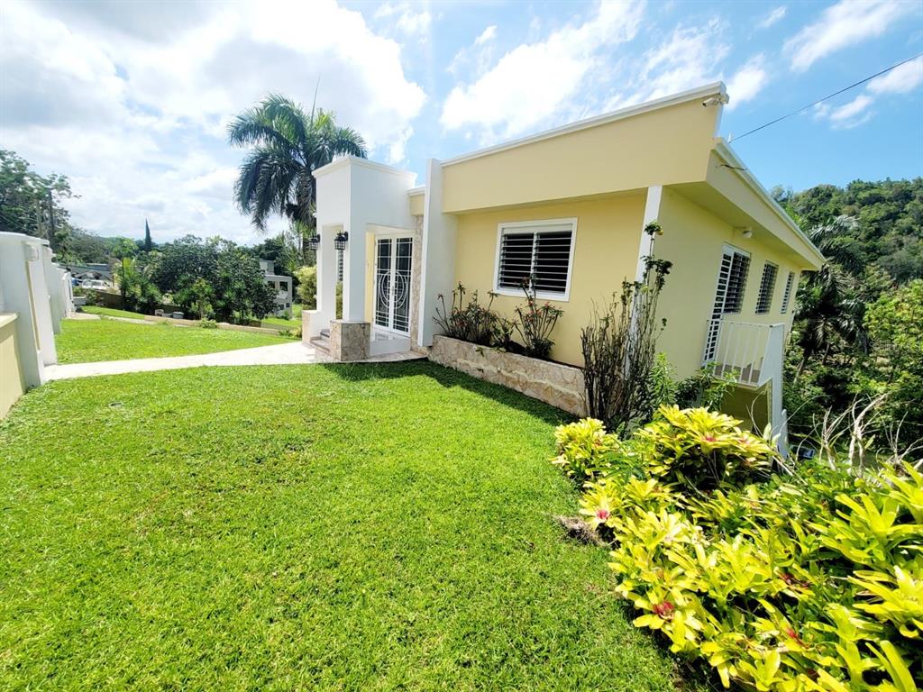 A yellow house with a white entryway and a green lawn under a blue sky — 8C CLAVEL ST., DORADO, PR