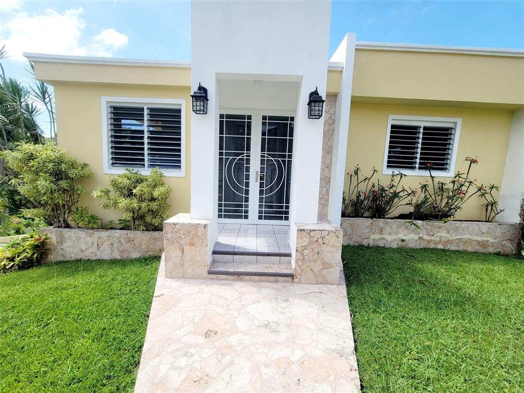 A yellow house exterior features a white entryway with double doors and a stone walkway — 8C CLAVEL ST., DORADO, PR