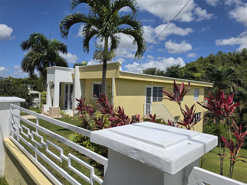 A yellow house with a white fence and palm trees under a blue sky — 8C CLAVEL ST., DORADO, PR