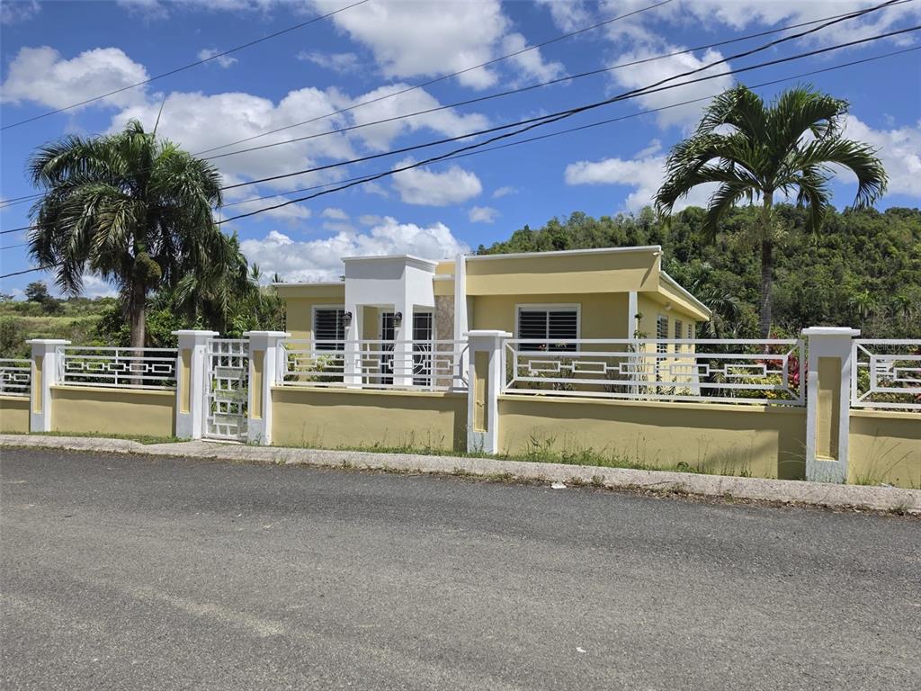 A yellow single-story house with a white fence and palm trees under a blue sky — 8C CLAVEL ST., DORADO, PR