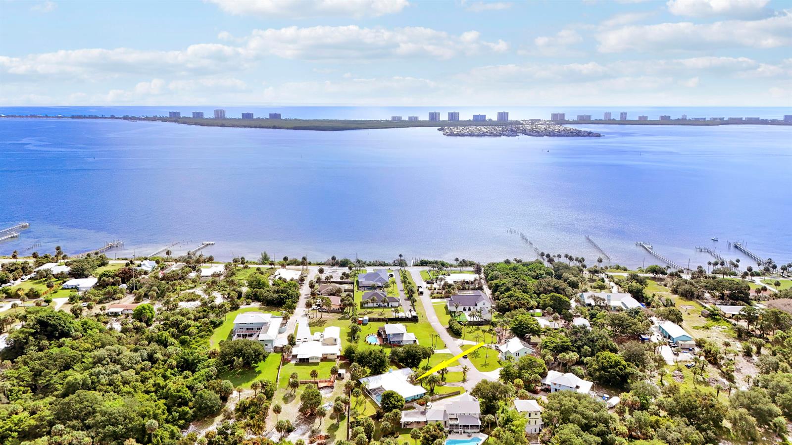 An aerial view shows a coastal neighborhood with houses, lush trees, and a large bay — 12744 Refuge Lane, Jensen Beach FL 34957, JENSEN BEACH, FL