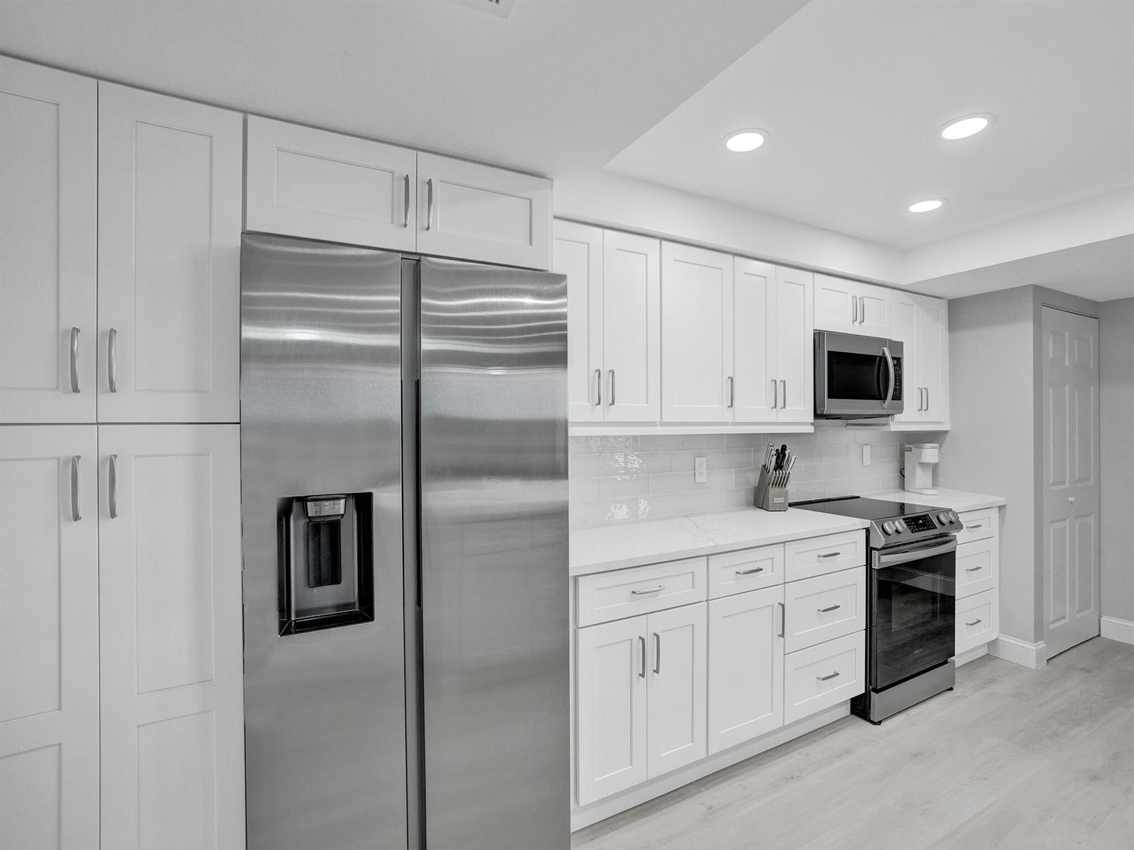 A modern kitchen features white cabinetry, stainless steel appliances, and light-colored countertops — 955 Egret Circle # 405, Delray Beach FL 33444, DELRAY BEACH, FL