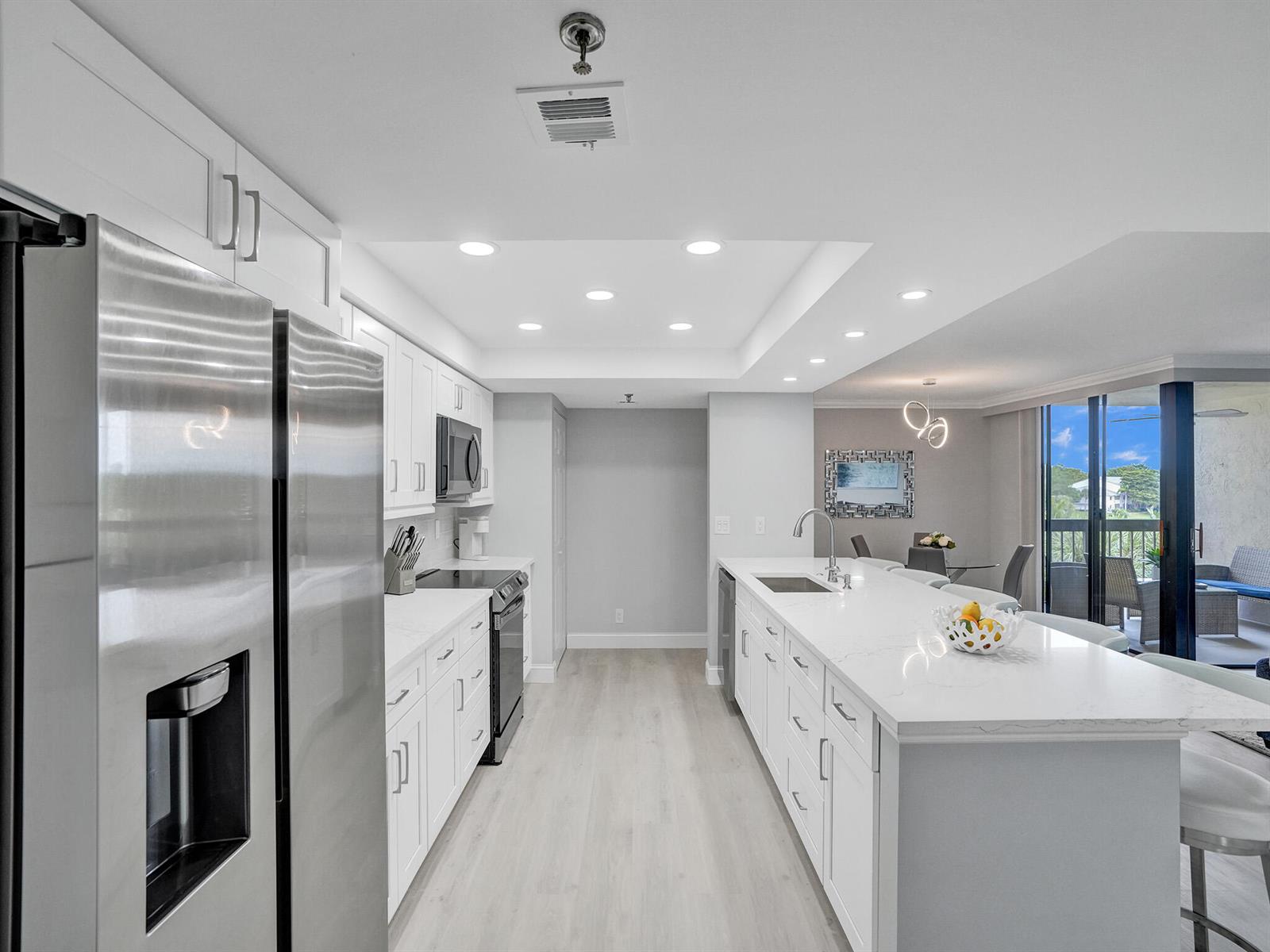 A modern kitchen features white cabinetry, stainless steel appliances, a large island, and light flooring — 955 Egret Circle # 405, Delray Beach FL 33444, DELRAY BEACH, FL