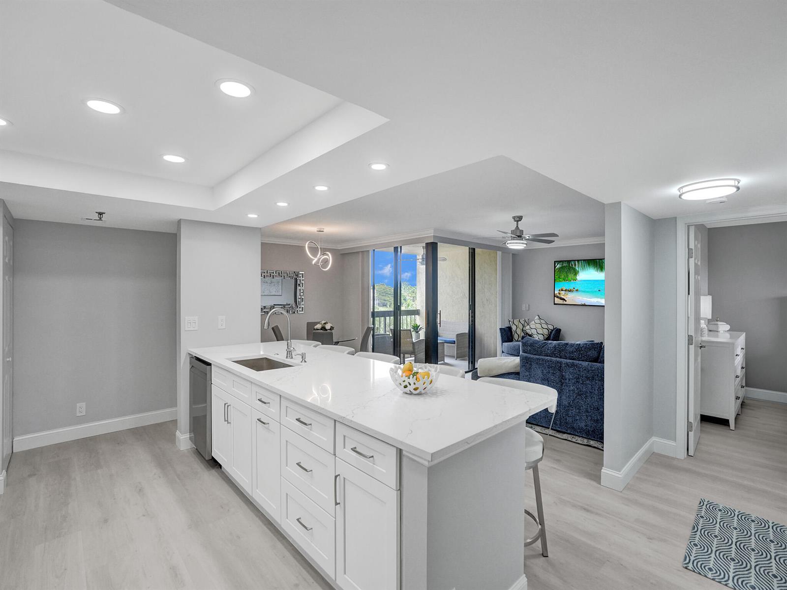 A white kitchen island with a sink sits in an open-concept living area with light flooring — 955 Egret Circle # 405, Delray Beach FL 33444, DELRAY BEACH, FL