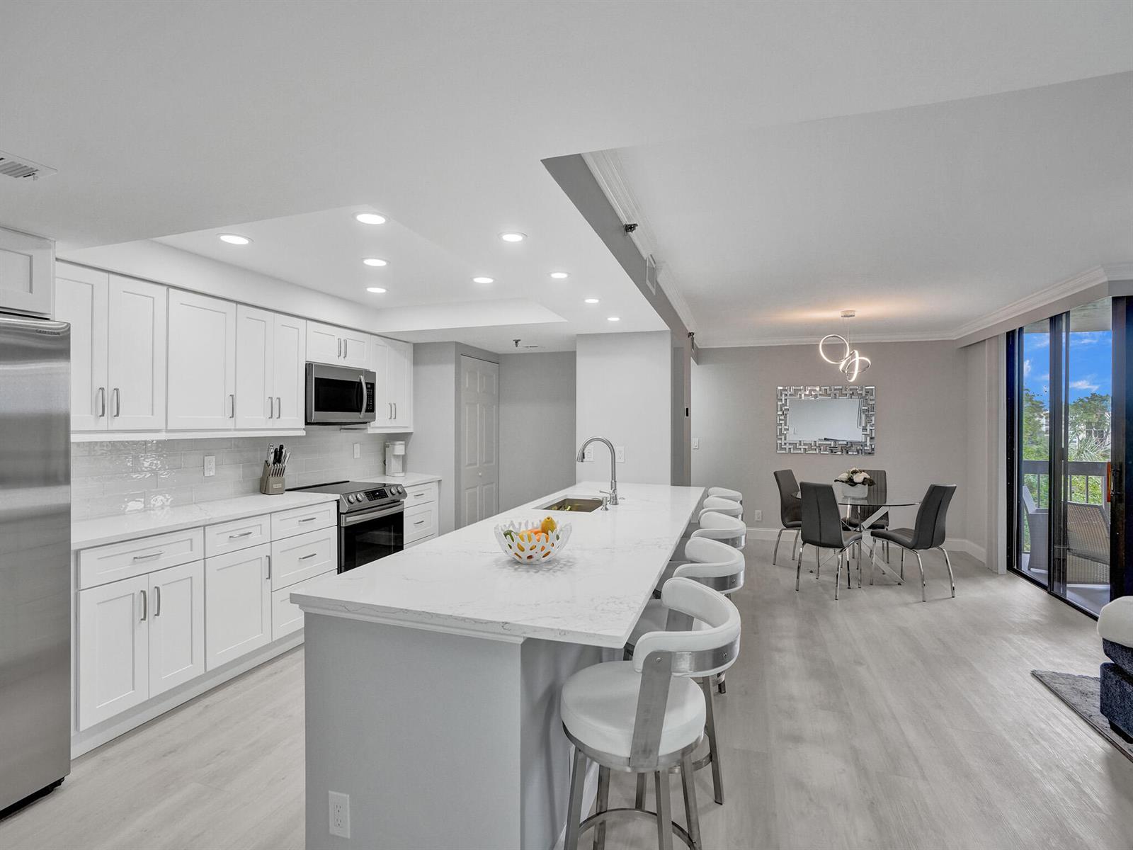 A modern kitchen with white cabinets, a marble-topped island, and an adjacent dining area — 955 Egret Circle # 405, Delray Beach FL 33444, DELRAY BEACH, FL