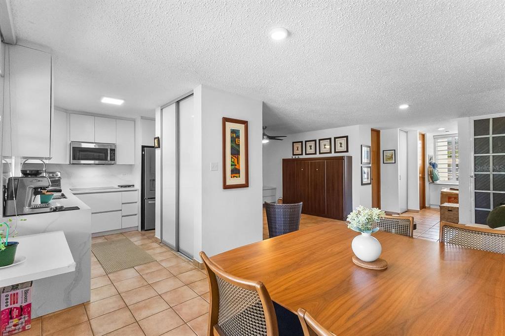 A dining area with a wooden table overlooks an open-concept kitchen with white cabinetry — 2306 CASA DEL MAR UNIT 2306, RIO GRANDE, PR