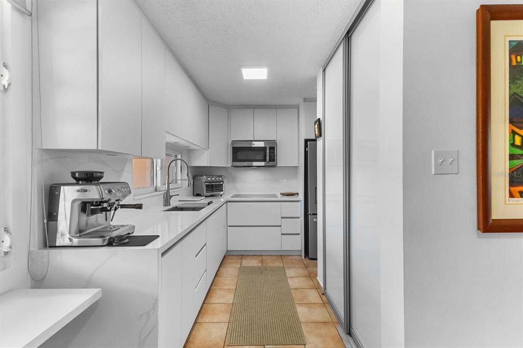 A modern white galley kitchen features sleek cabinetry, quartz countertops, and stainless steel appliances — 2306 CASA DEL MAR UNIT 2306, RIO GRANDE, PR