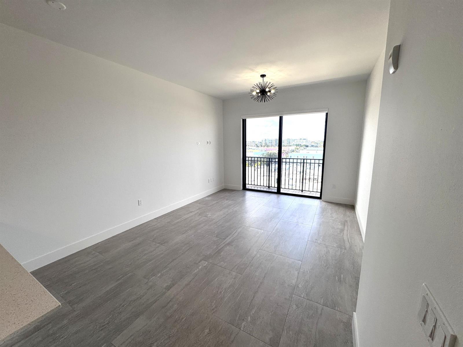 A bright, empty living room features large gray floor tiles, white walls, and a balcony — 511 Lucerne Avenue # 611, FL 33460, FL