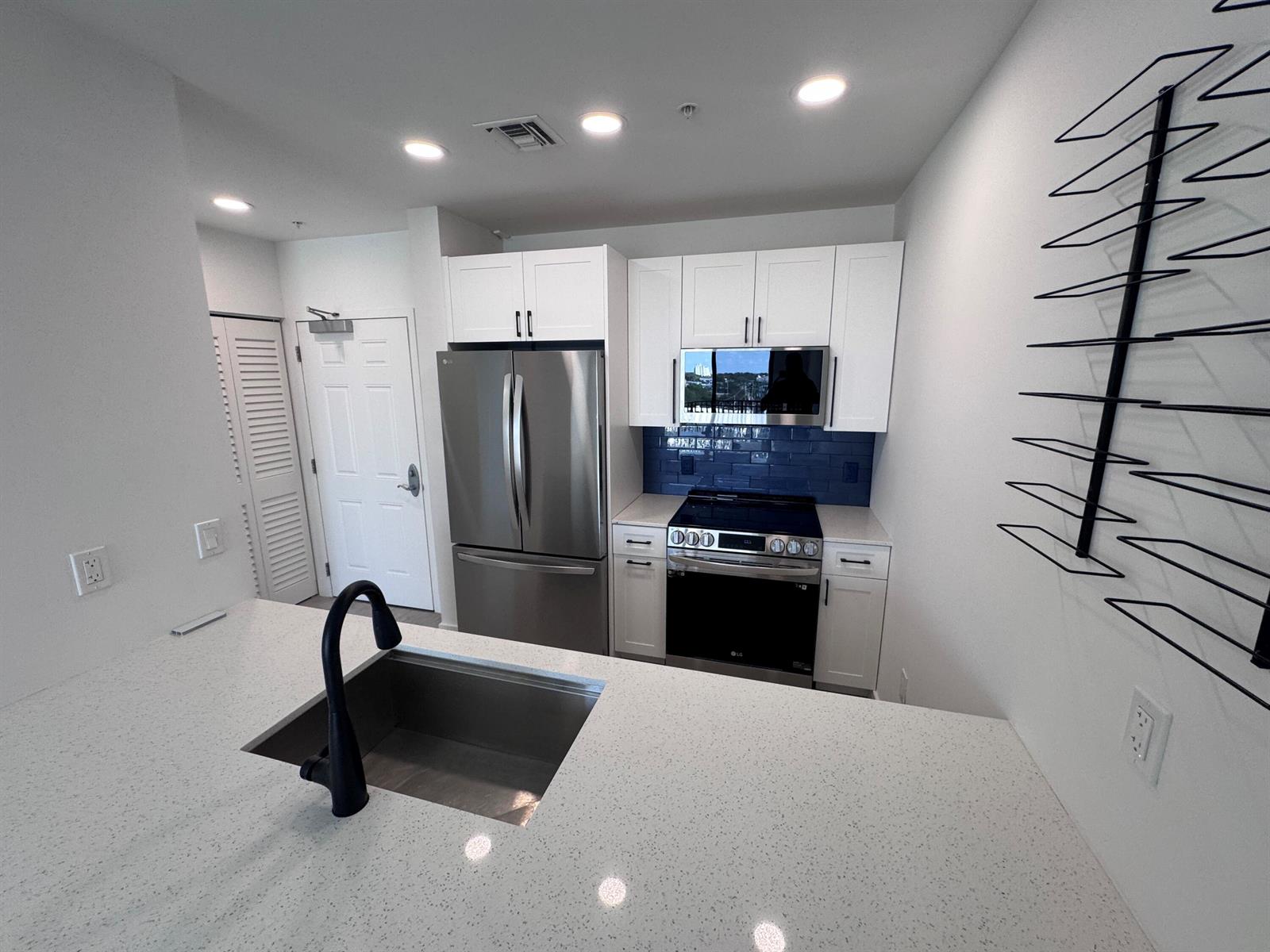 A kitchen features white cabinets, stainless steel appliances, a blue tile backsplash, and a quartz island — 511 Lucerne Avenue # 611, FL 33460, FL