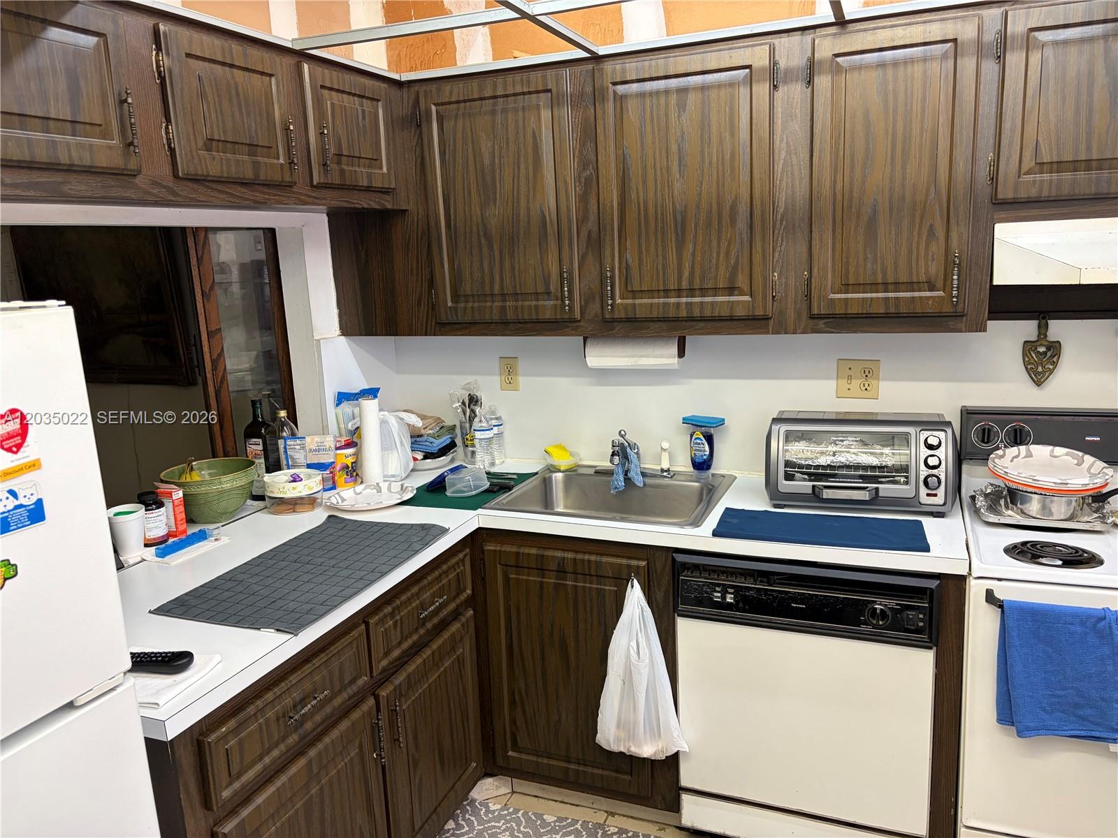 A kitchen features dark wood cabinets, white countertops, a stainless steel sink, and white appliances — 1655 NE 115th St # 29B, Miami FL 33181, MIAMI, FL