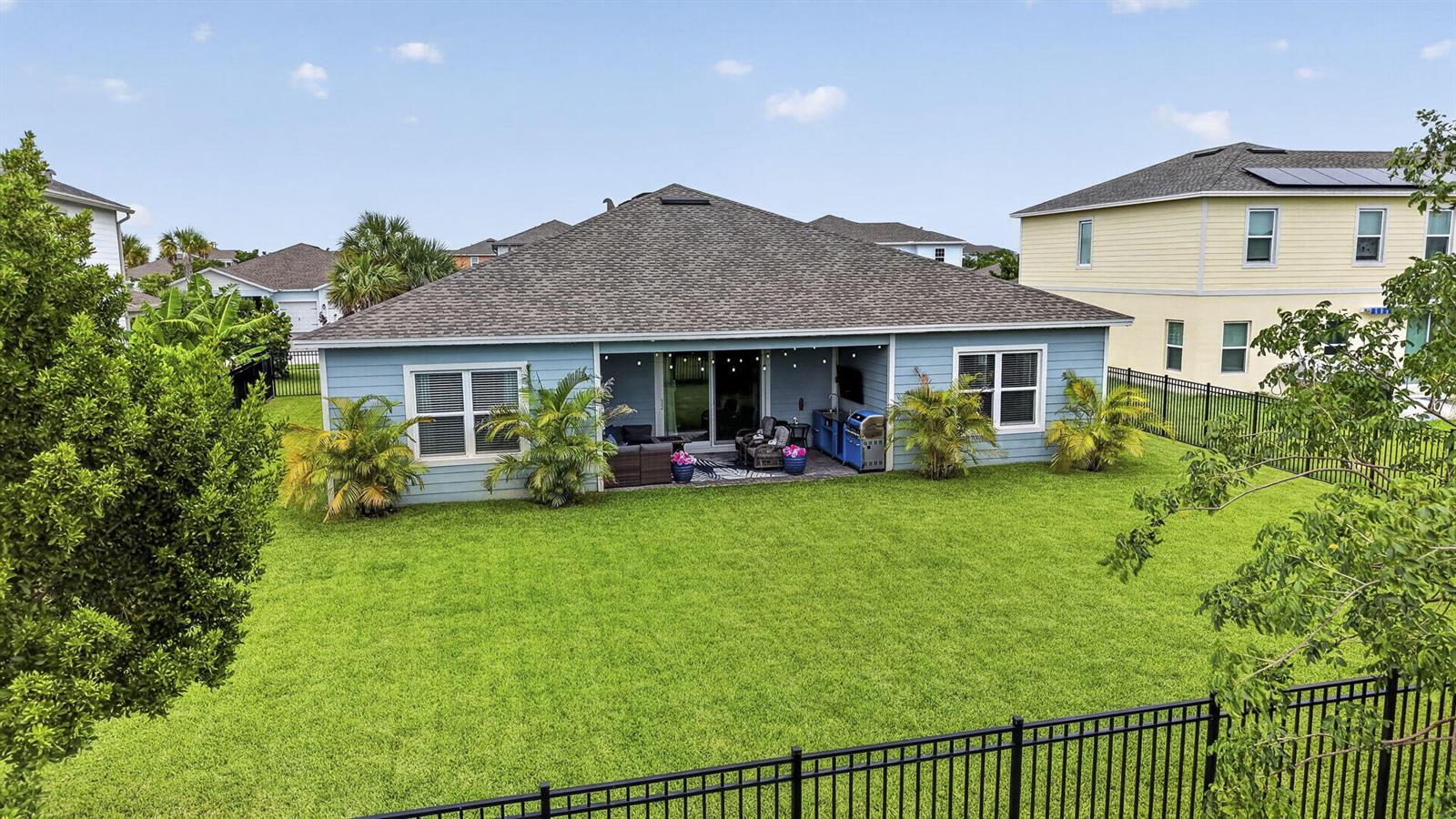 The exterior rear view of a blue house features a covered patio and fenced yard — 1201 Harvester Crossing, Loxahatchee FL 33470, LOXAHATCHEE, FL