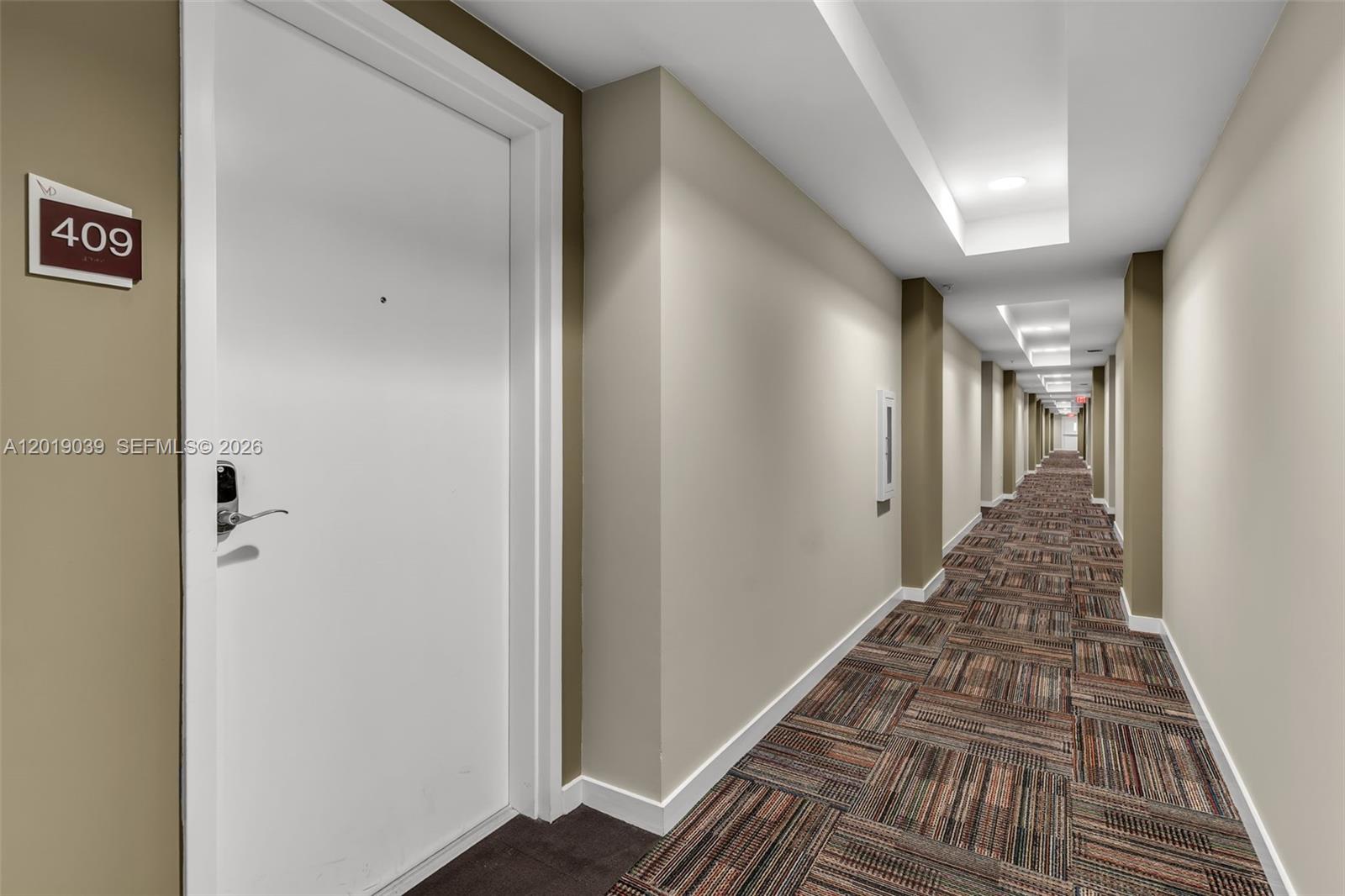 A long, carpeted apartment hallway features a white door labeled 409 on the left — 7661 NW 107th Ave # 409, Doral FL 33178, DORAL, FL
